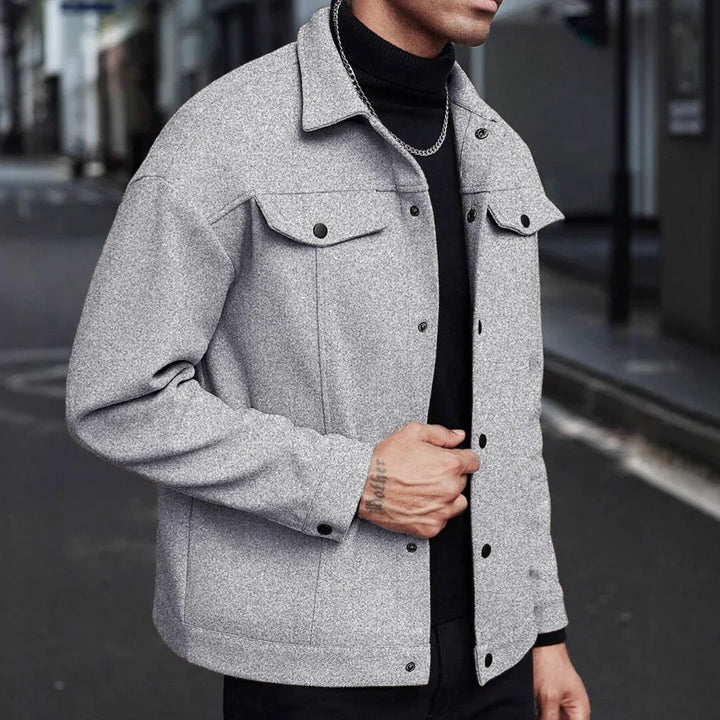 Man wearing a stylish light gray wool jacket over black turtleneck and silver chain necklace on urban street