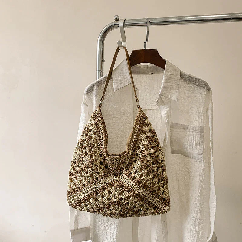 Crochet woven handbag with leather strap hanging on a white textured button-up shirt on a metal clothing rack