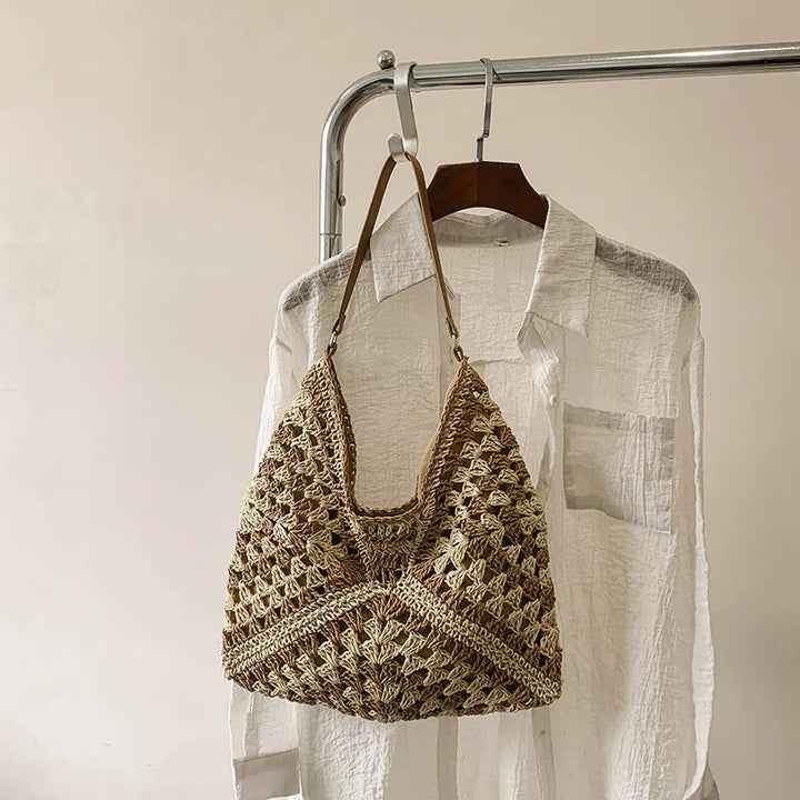 Crochet woven handbag with leather strap hanging on a white textured button-up shirt on a metal clothing rack