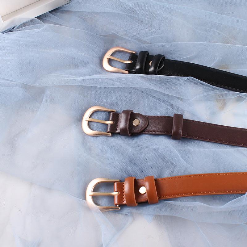 Three leather belts in black, dark brown, and tan with gold buckles on blue sheer fabric