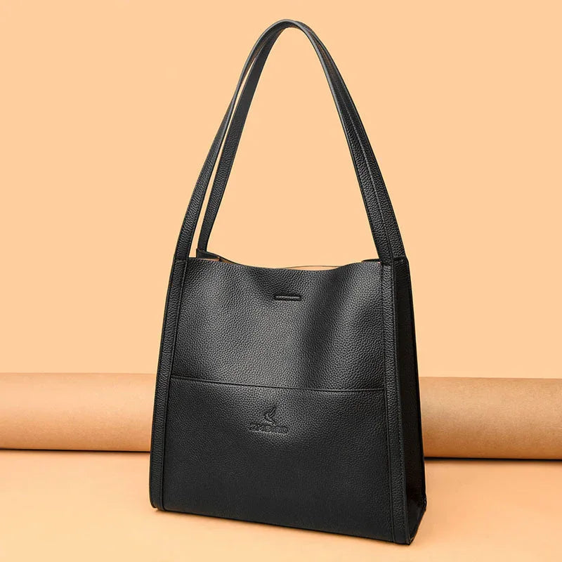 Black leather tote bag with dual handles and embossed logo on peach background