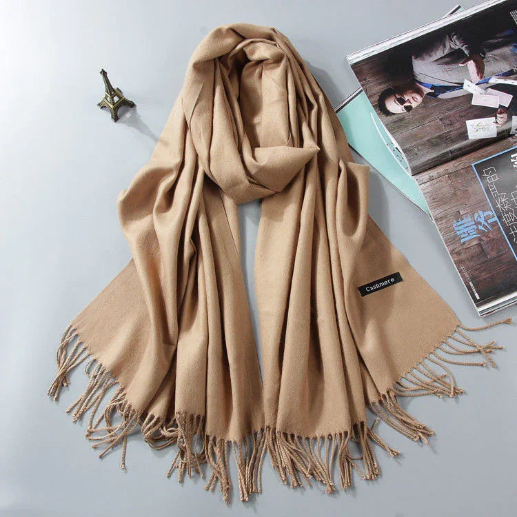 Beige cashmere scarf with fringed edges laid flat next to a mini Eiffel Tower model and opened magazine