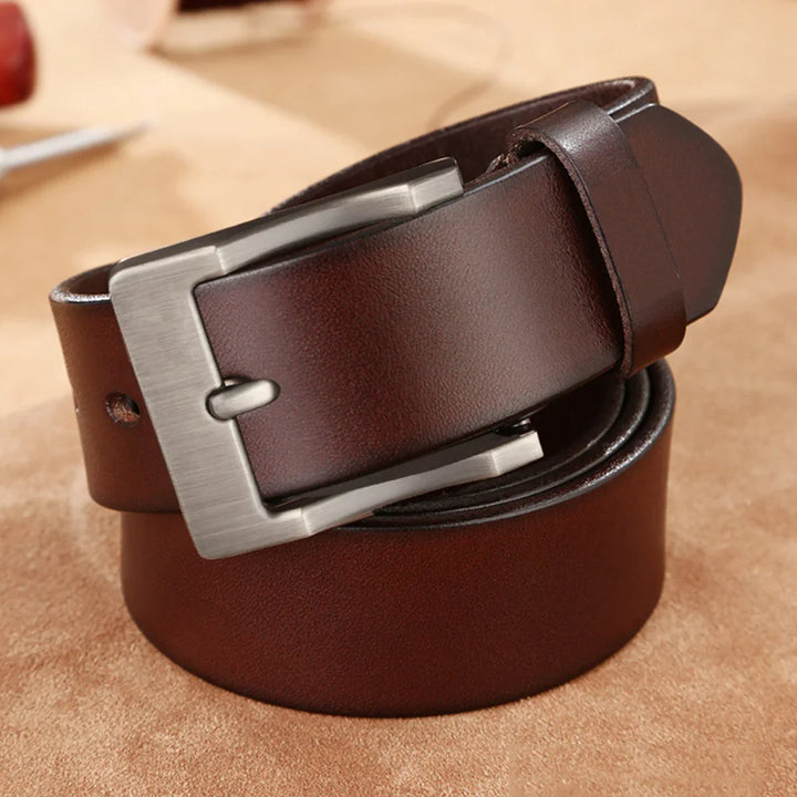Close-up of a rolled dark brown leather belt with a brushed silver buckle on a suede surface