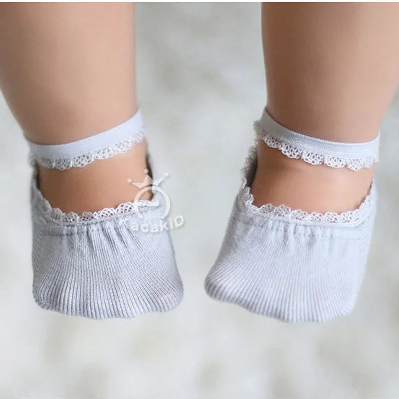 Baby feet wearing soft gray ankle socks with lace trim on a white background