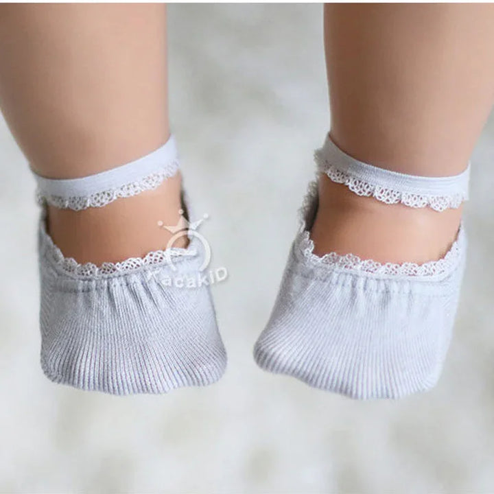 Baby feet wearing soft gray ankle socks with lace trim on a white background
