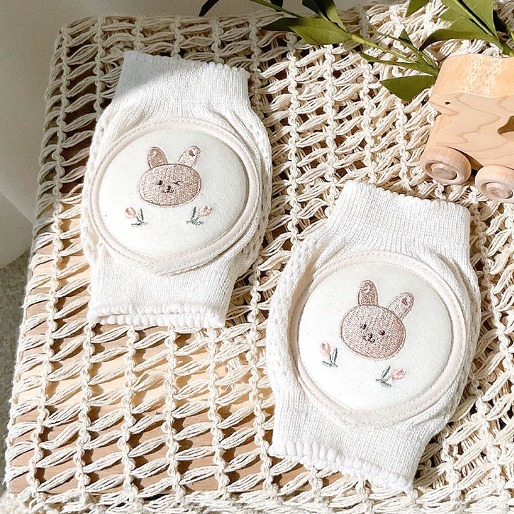 White knit baby knee pads with embroidered cute bunny and flower design on woven mat