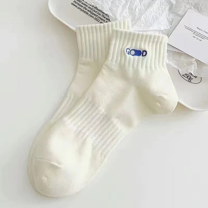 Pair of white ribbed ankle socks with blue 'GOOD' logo on a white surface
