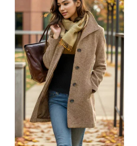 Woman in brown wool coat, beige scarf, and blue jeans walking outdoors on autumn day