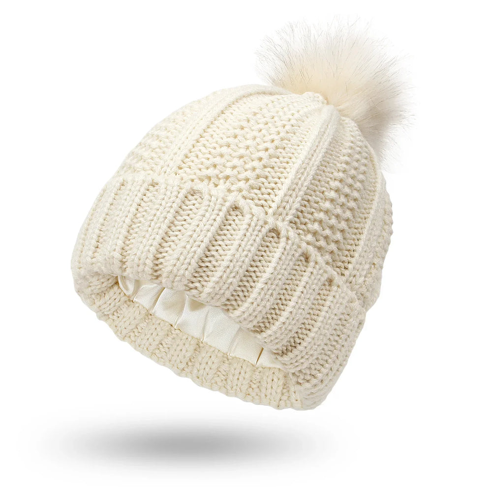 Cream knit beanie hat with pom-pom and satin-lined interior for winter warmth