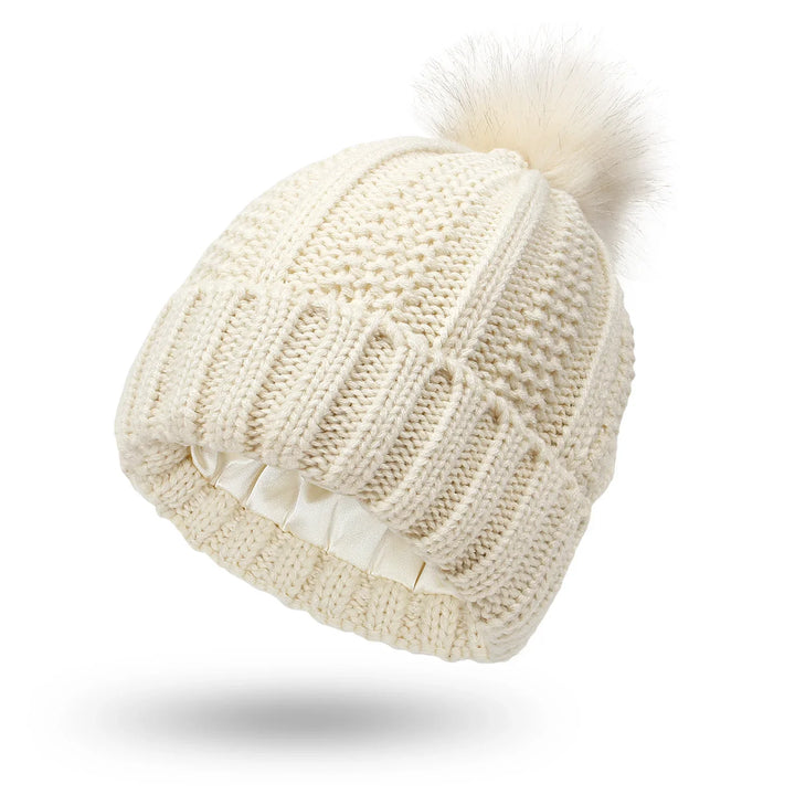 Cream knit beanie hat with pom-pom and satin-lined interior for winter warmth