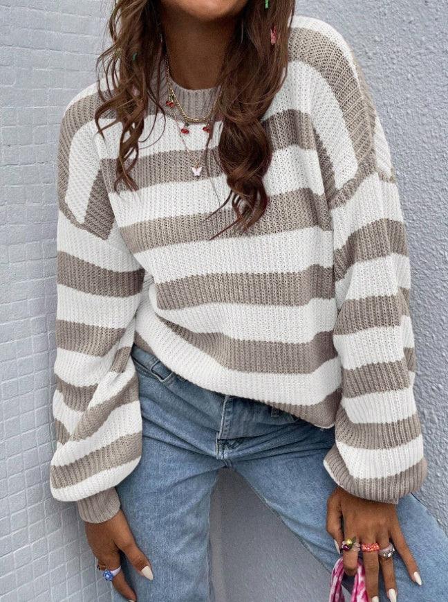 Woman wearing beige and white striped knit sweater with blue jeans and colorful rings against gray wall