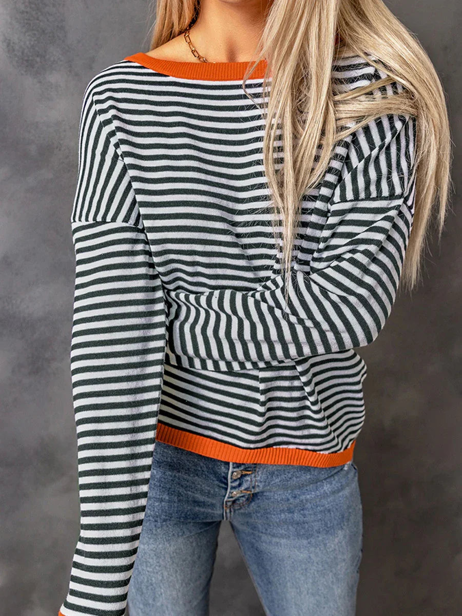 Woman wearing black and white striped long sleeve top with orange trim and blue jeans against gray background