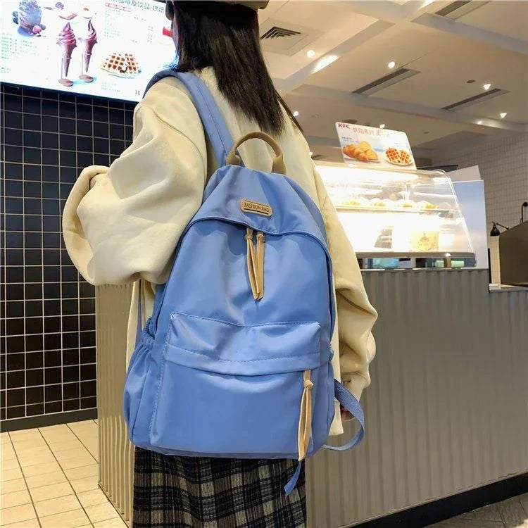 Person wearing beige sweater and plaid skirt carrying light blue backpack inside a cafe next to display counter