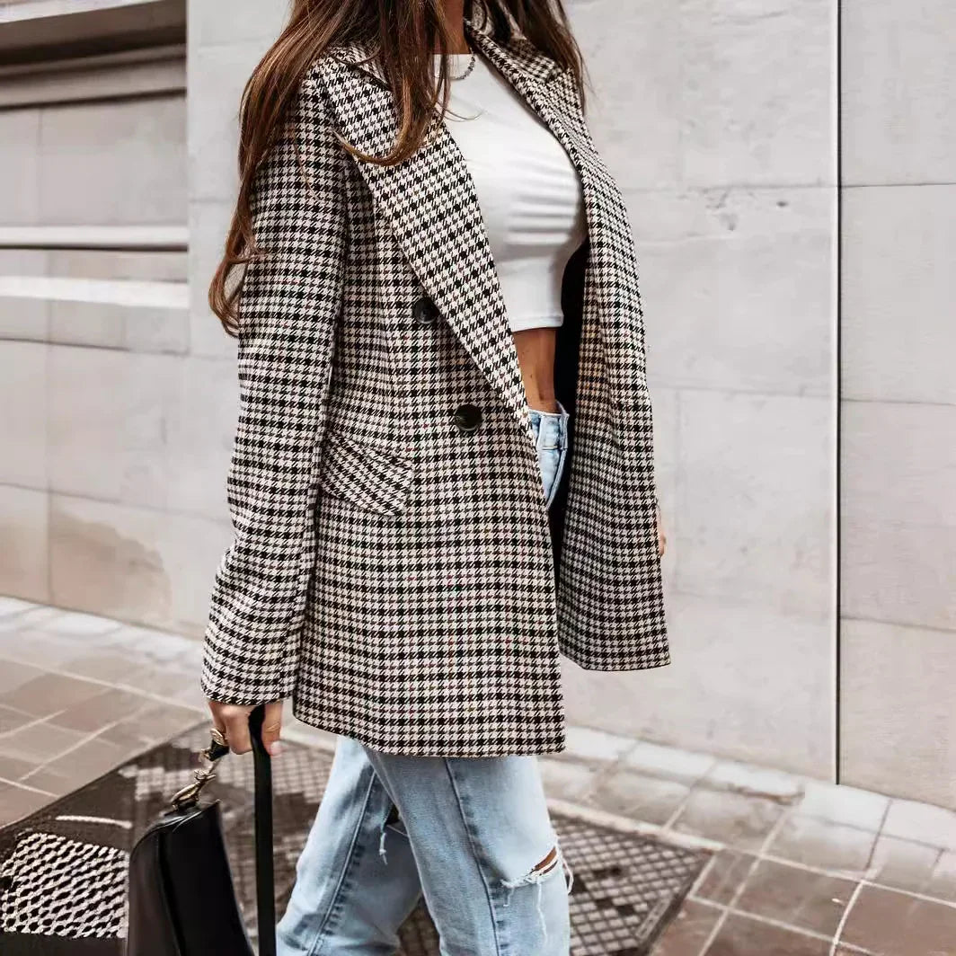 Woman wearing black and white houndstooth blazer, white crop top, ripped jeans, holding black handbag on city sidewalk