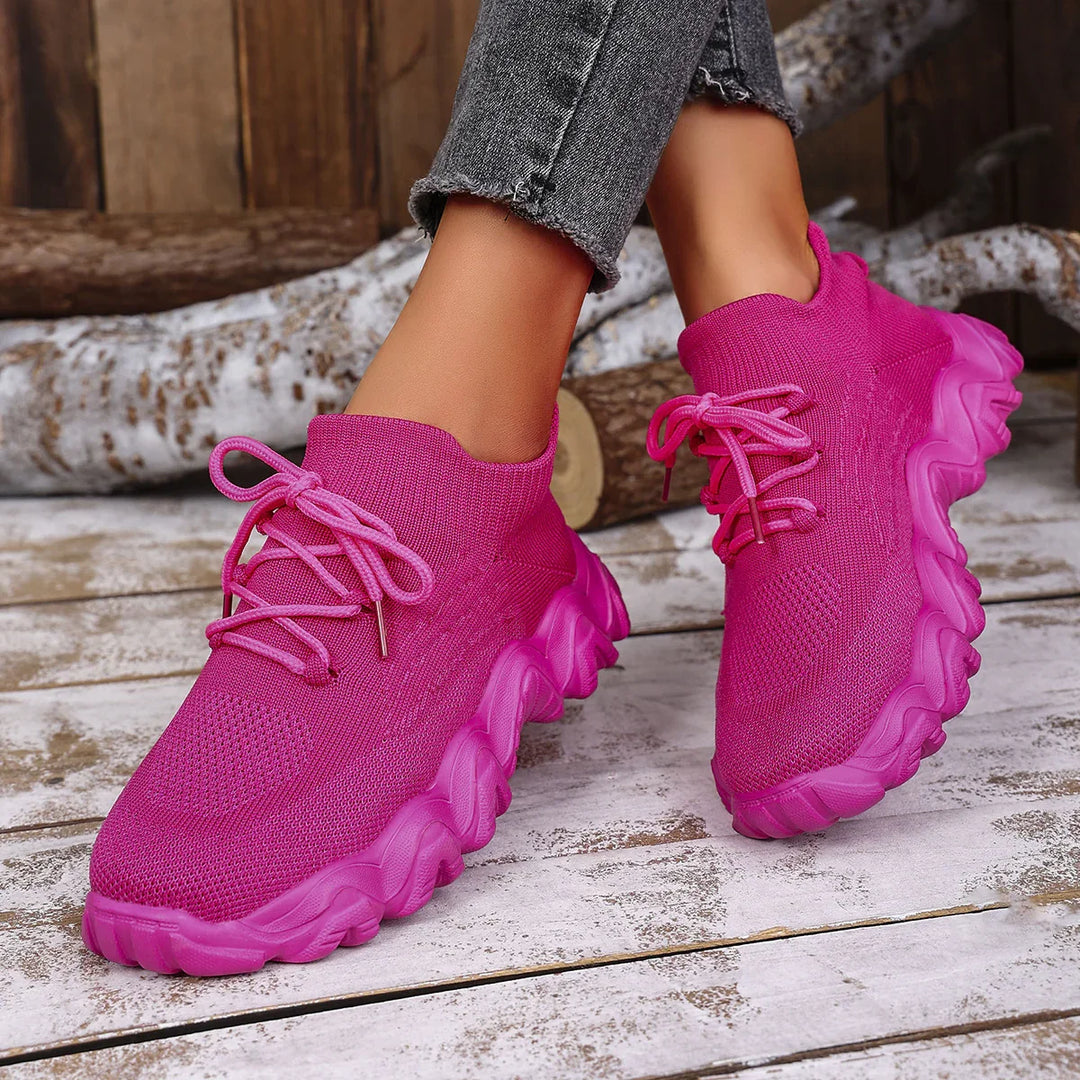 Bright pink knitted sneakers with chunky soles worn with cropped grey jeans on wooden floor