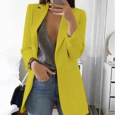 Woman wearing bright yellow blazer over deep V-neck gray top and blue jeans, taking mirror selfie