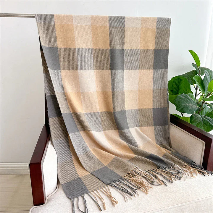 Beige and gray plaid throw blanket draped over beige armchair with wooden arms, green plant in background