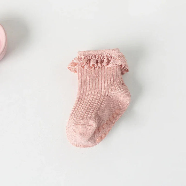 Pink baby sock with ruffled lace cuff and non-slip dots on white background