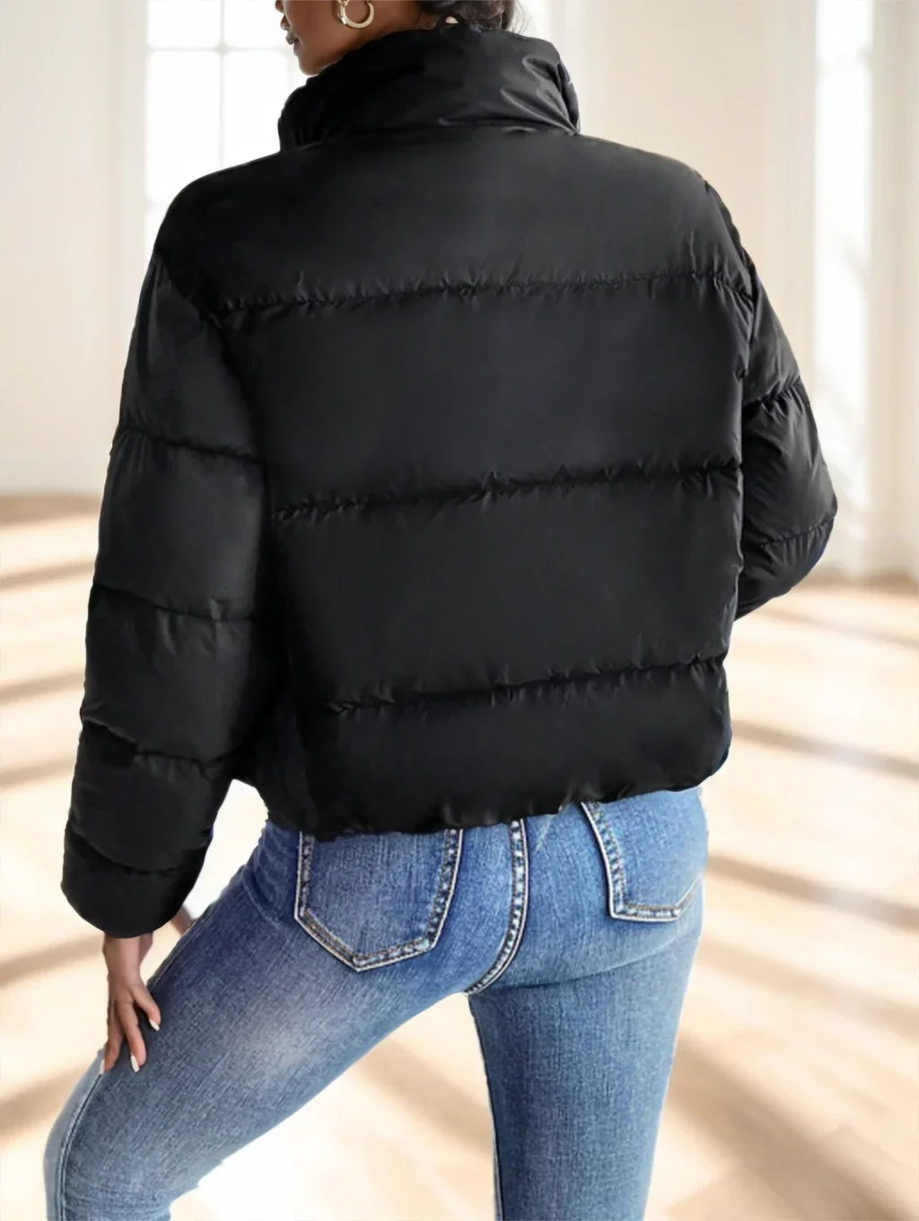 Back view of woman wearing black puffer jacket and blue denim jeans in bright room