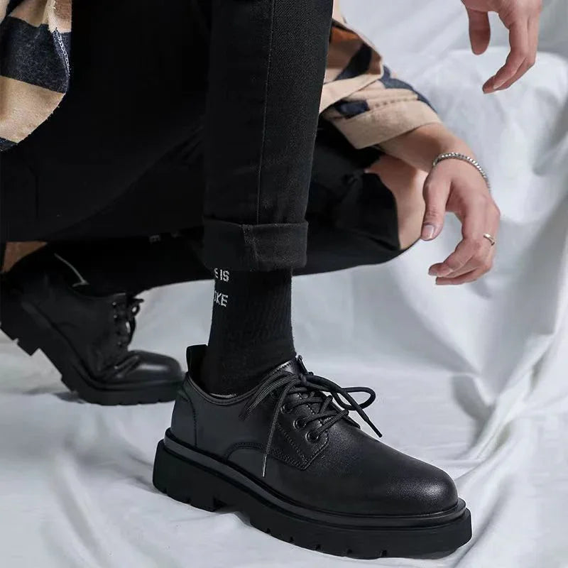 Person wearing black chunky leather shoes with black pants and black socks on light fabric background