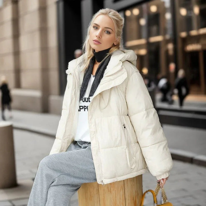 Young woman in white puffer jacket and gray pants sitting on wooden stool in urban street
