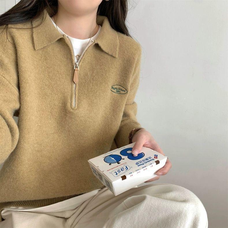 Person wearing camel wool zip-up sweater holding white Domino's pizza box against plain background