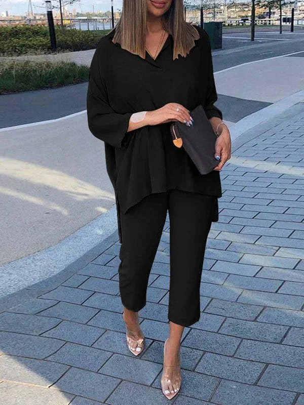 Woman in stylish loose black top and cropped pants walking on paved urban path holding black clutch