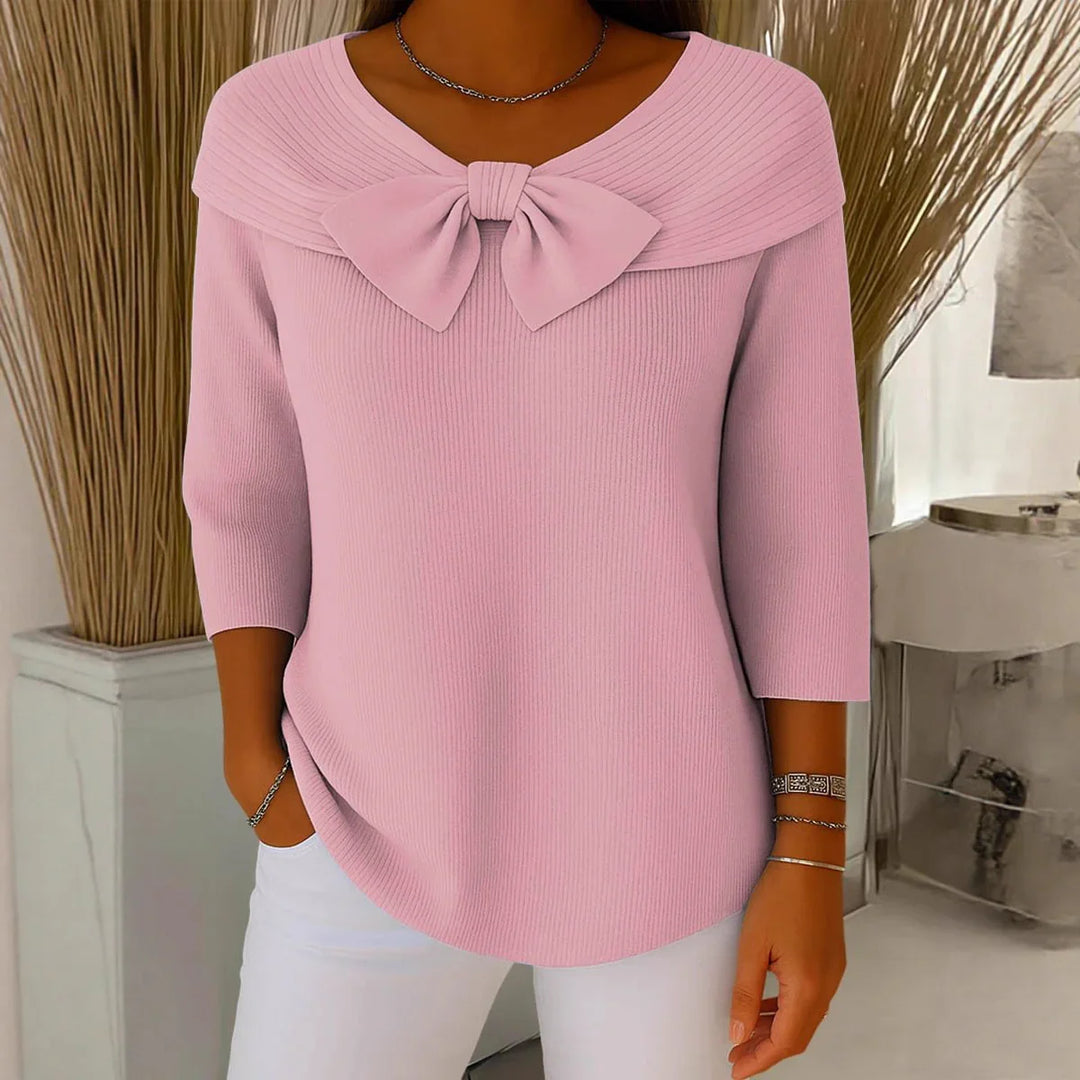 Woman wearing pink ribbed sweater with bow detail and three-quarter sleeves, paired with white pants