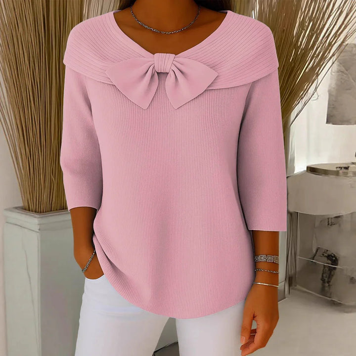 Woman wearing pink ribbed sweater with bow detail and three-quarter sleeves, paired with white pants