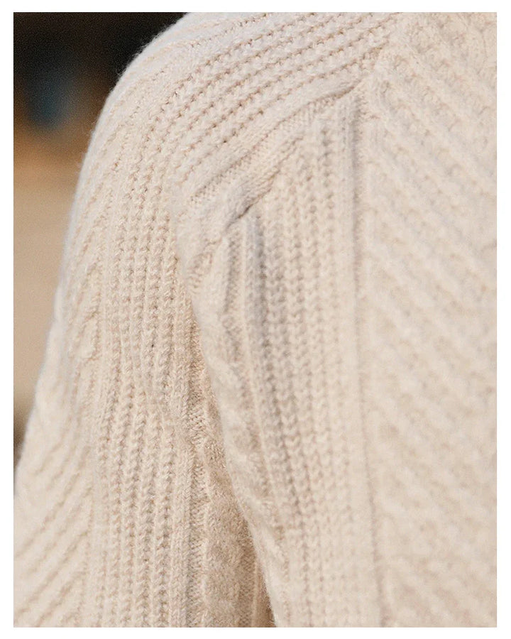 Close-up of beige cable knit wool sweater shoulder, showing textured knit pattern and soft fabric