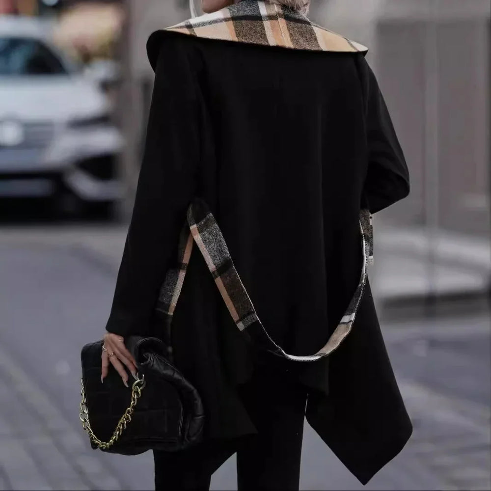 Woman wearing black asymmetrical coat with plaid collar and belt, holding black handbag with gold chain on city street