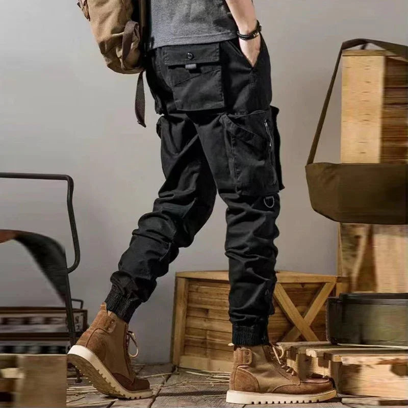 Person wearing black cargo pants and brown lace-up boots in rustic setting with wooden crates