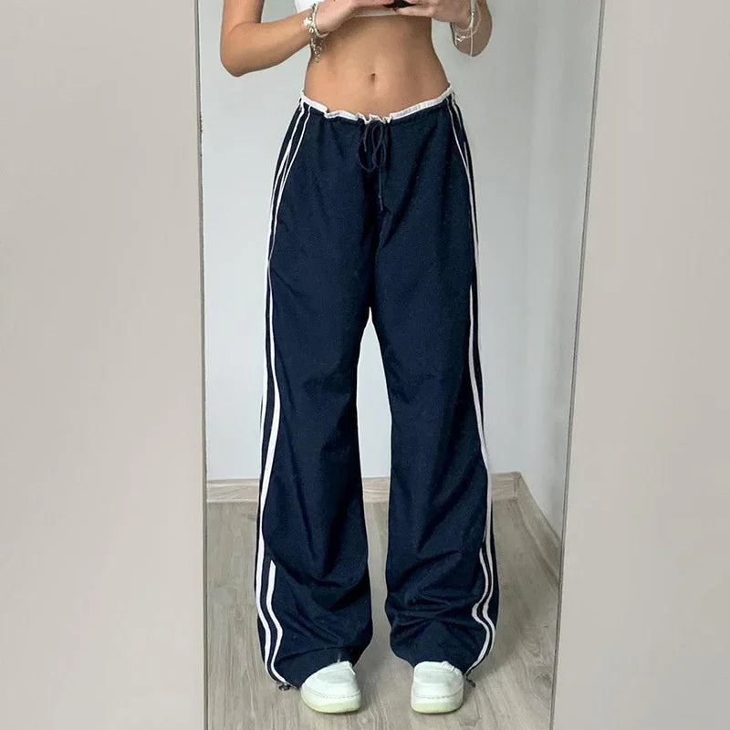 Person wearing navy blue wide-leg track pants with white stripes and white sneakers, standing indoors