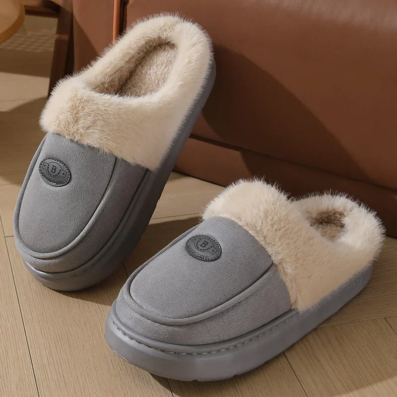 Gray cozy indoor slippers with plush cream fur lining on wooden floor by brown sofa