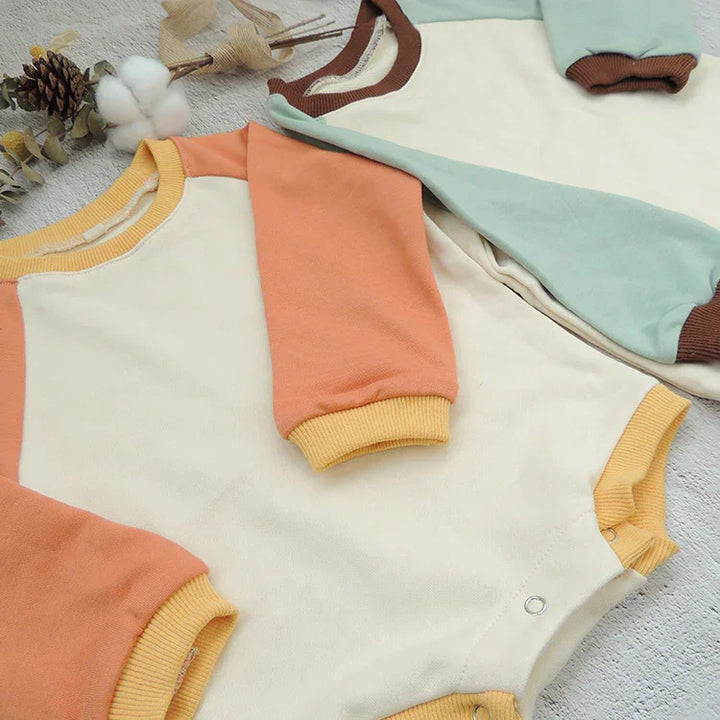 Two color-blocked baby onesies with snap closures, one with orange and yellow sleeves, another with mint green and brown sleeves