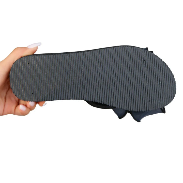 Hand holding black sole of a flat shoe with ridged textured bottom against white background