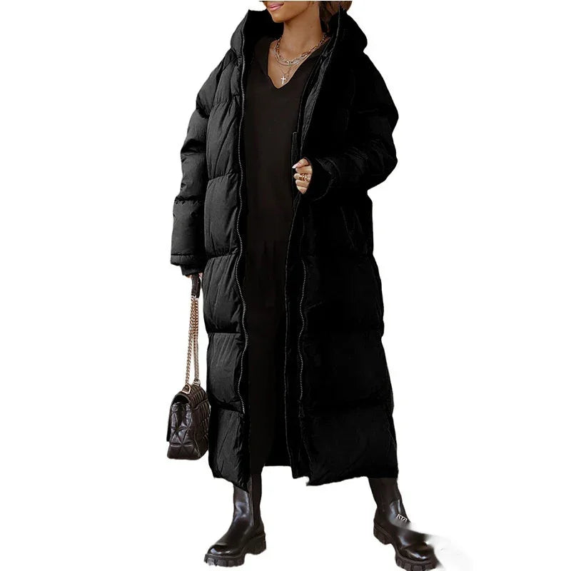 Woman wearing long black puffer coat with hood, black boots, holding quilted handbag with chain strap