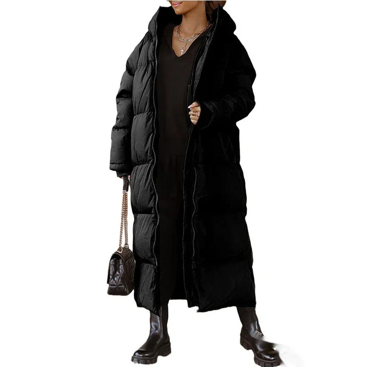 Woman wearing long black puffer coat with hood, black boots, holding quilted handbag with chain strap