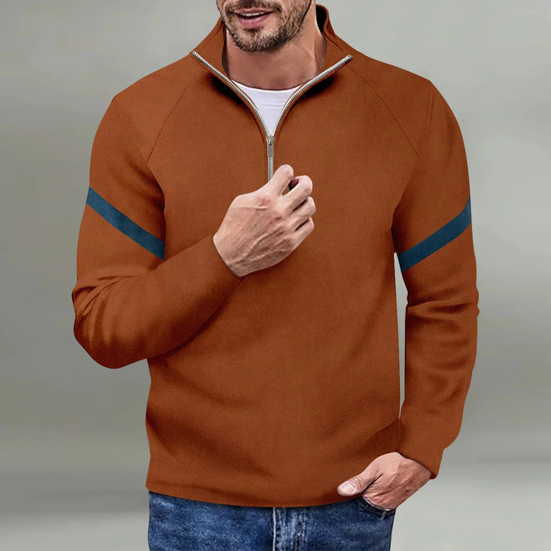 Man wearing a brown quarter-zip pullover with navy stripes on sleeves and blue jeans