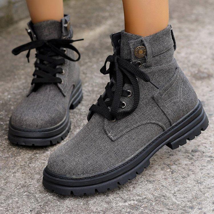 Close-up of gray fabric ankle boots with black laces on textured outdoor ground