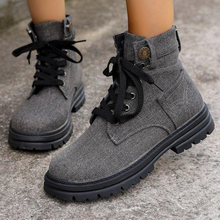 Close-up of gray fabric ankle boots with black laces on textured outdoor ground