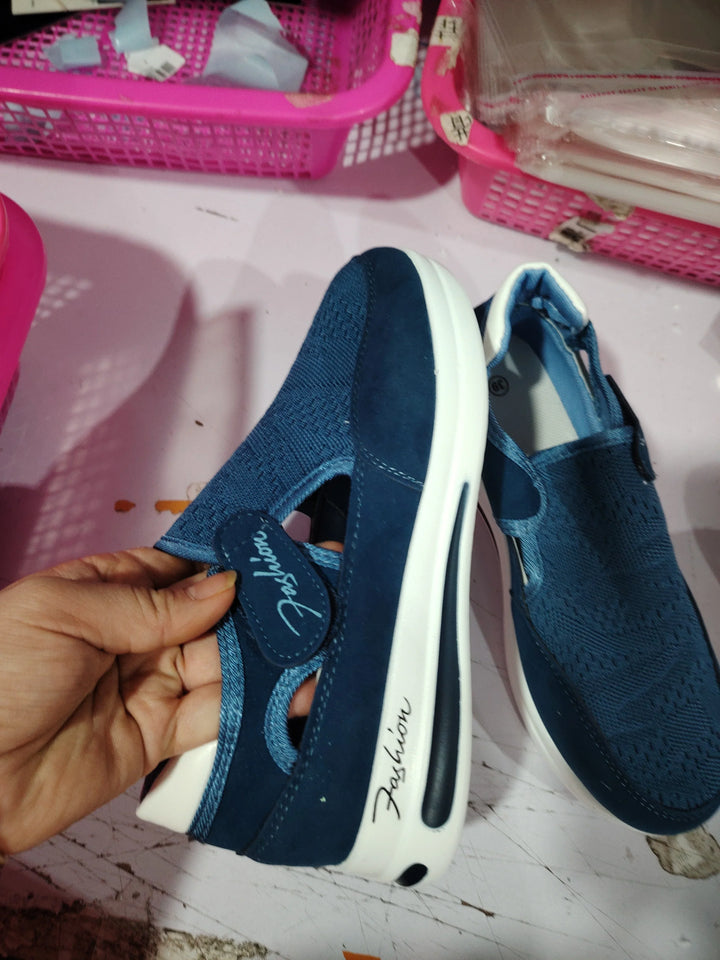Blue casual slip-on shoes with white soles and 'Fashion' text, held by hand on pink surface