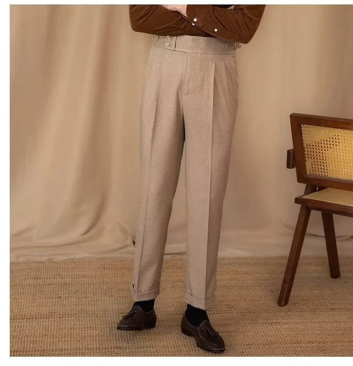 Man wearing beige pleated trousers with cuffed hems, black socks, and brown loafers in a neutral setting