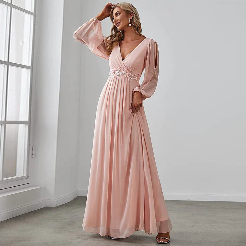Woman in elegant blush pink long sleeve evening gown with floral waist embellishment