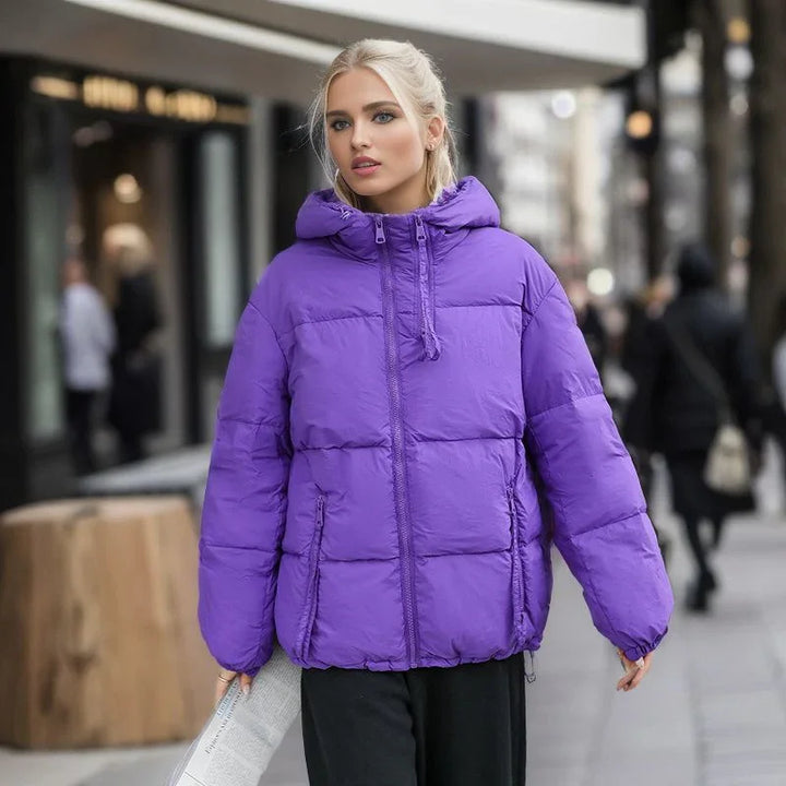 Young woman wearing a purple puffer jacket with hood walking in urban street setting