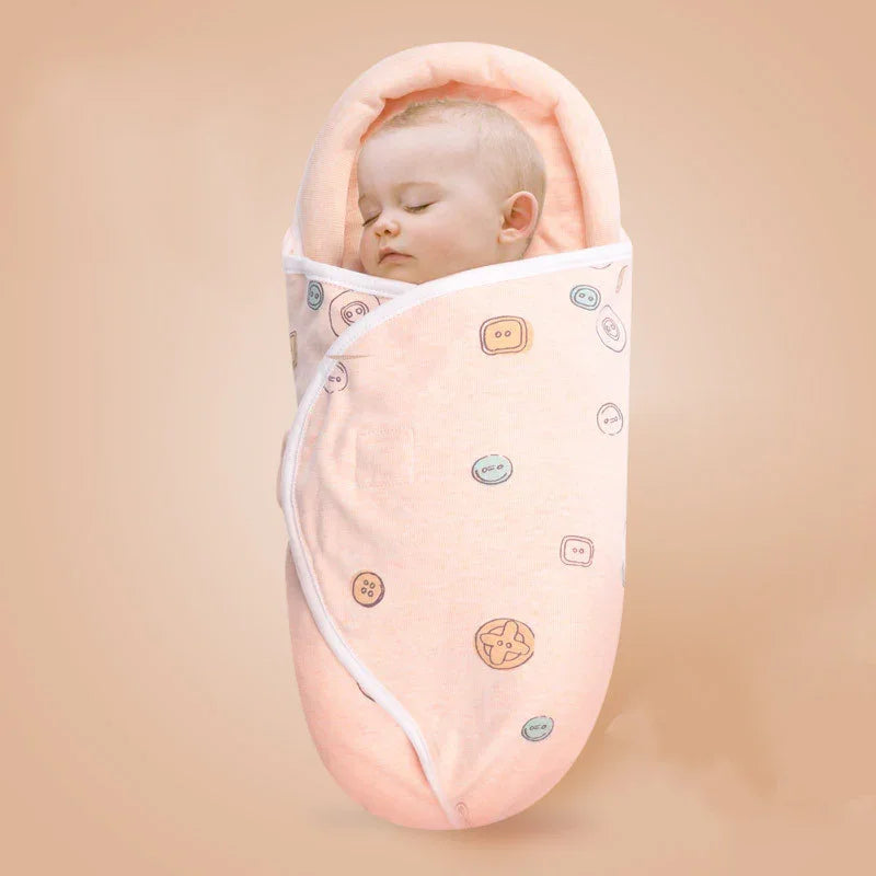 Sleeping baby swaddled in peach baby wrap with button prints on neutral beige background