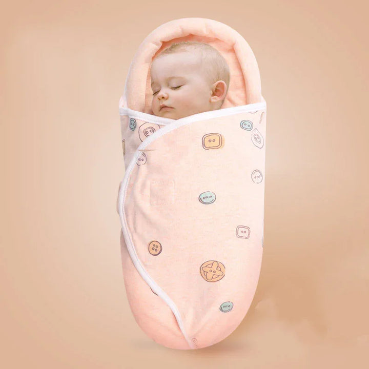 Sleeping baby swaddled in peach baby wrap with button prints on neutral beige background