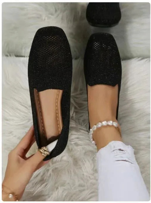 Black sparkling flat shoes worn on feet with white ripped jeans and pearl anklet on a fluffy white rug