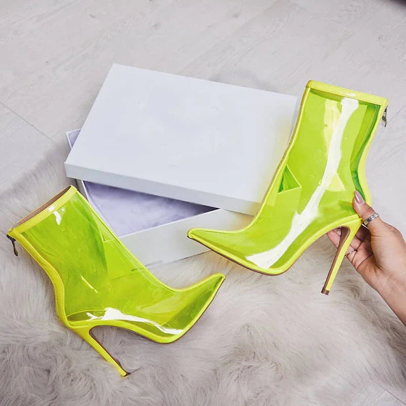 Pair of neon yellow transparent high heel ankle boots with pointed toes on a white fur rug