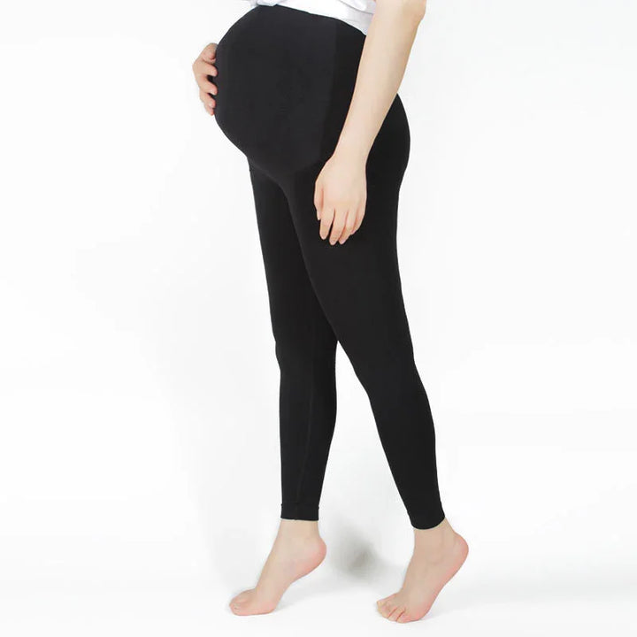 Pregnant woman wearing black maternity leggings standing barefoot on white background